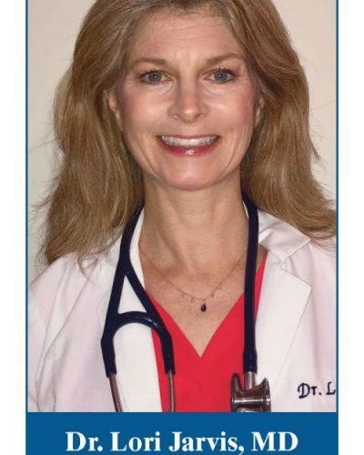 Headshot of Dr. Loris Jarvis. Dr. stares straight and smiles. She has long dark blond hair and wears a red shirt, white lab coat and a stethoscope around her neck.