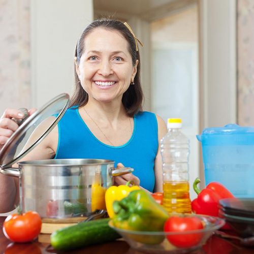 Happy woman cooking with vegetables at her kitchen at home