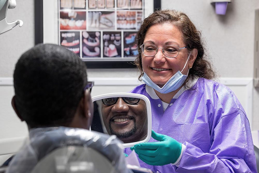 Man in dental chair smiling in mirror held by dentist